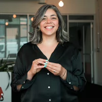 A smiling woman in a black shirt stands in a bright, modern office setting.