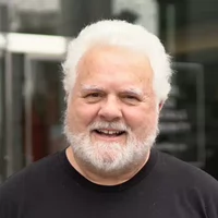 Smiling older man with a white beard and hair, wearing a black shirt.